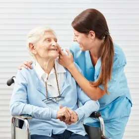 A smiling caregiver with an elderly woman in a wheelchair