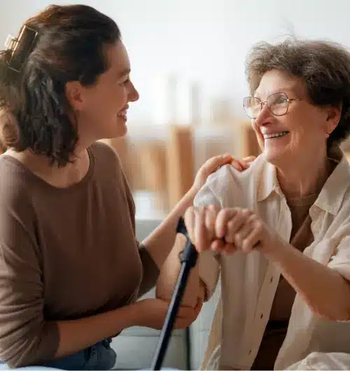 A caregiver talks with a smiling older woman holding a cane.